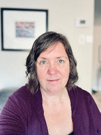 Woman with shoulder-length brown hair wearing a purple sweater in an indoor setting.